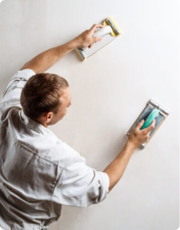 Painter sanding a wall with two sanding blocks